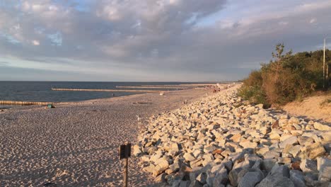 Sandstrand-In-Mielno,-Polen-Bei-Wunderschönem-Sommersonnenuntergang-Mit-Steinbarrieren