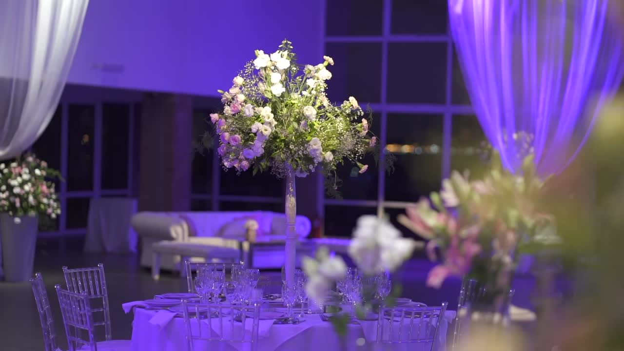 Panning shot showing a tall wedding floral centerpiece and soft blue lighting with flowers in foreground