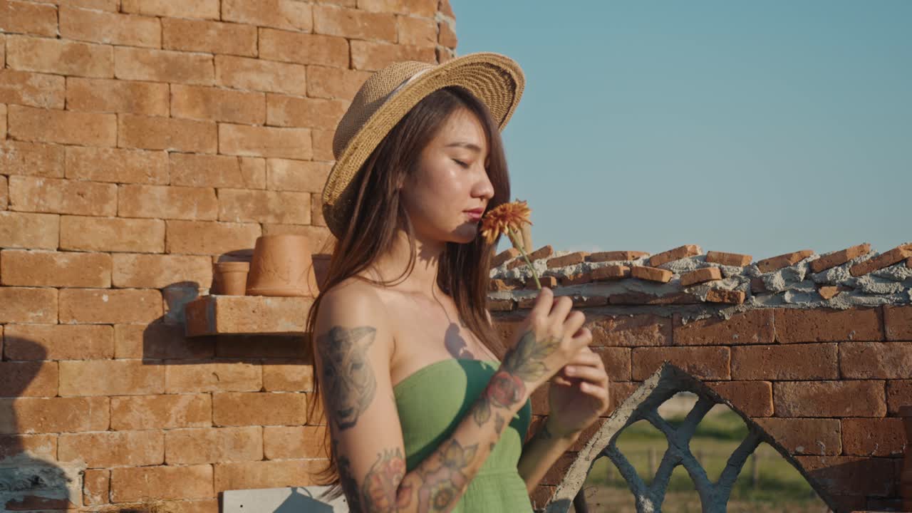 Woman with flower and straw hat by brick wall