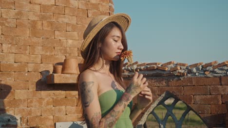 woman with flower and straw hat by brick wall