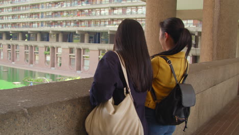 Rear-View-Of-Two-Young-Female-Friends-Visiting-The-Barbican-Centre-In-City-Of-London-Taking-Photo-On-Mobile-Phone-1