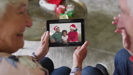 Pareja-Caucásica-Mayor-Usando-Tableta-Para-Videollamada-Navideña-Con-Familia-Feliz-En-La-Pantalla