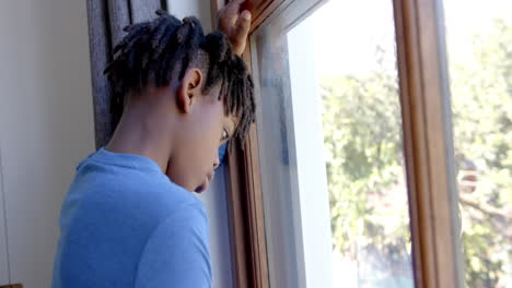thoughtful african american boy looking through window at home, slow motion