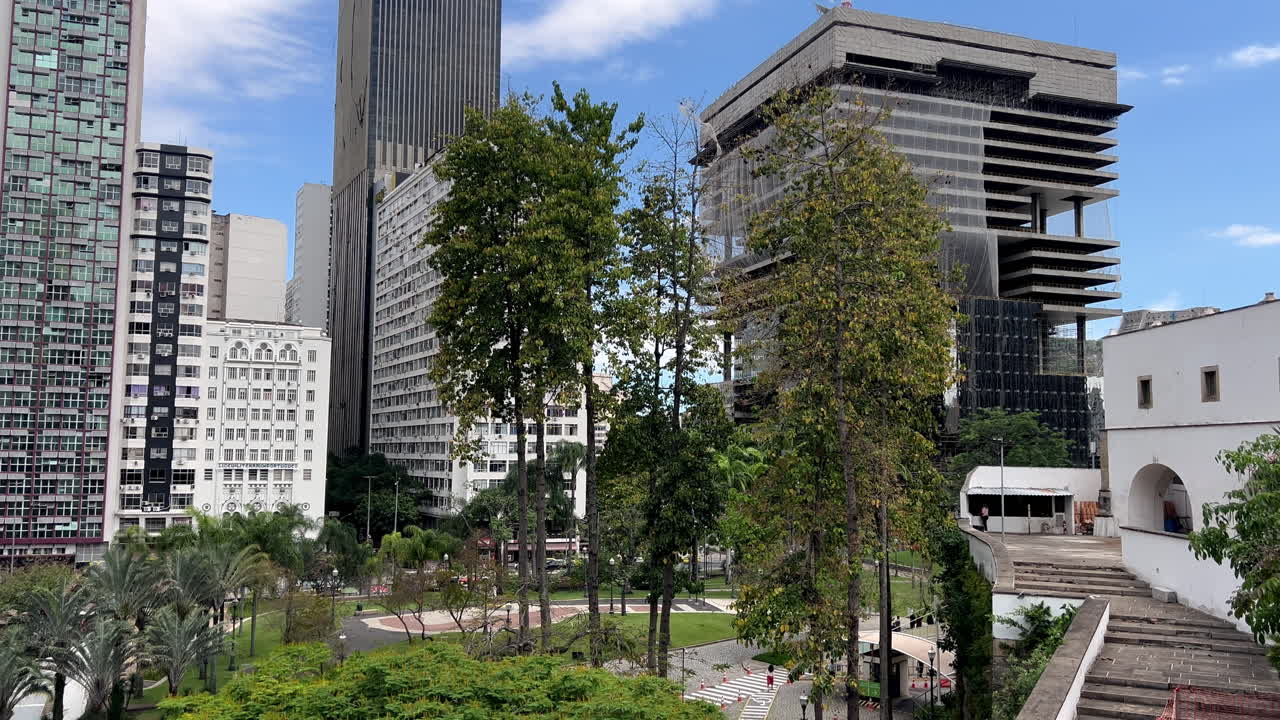 A sharp contrast of nature and commerce in Rio's financial district. The scene captures modern high-rise office buildings, including the Petrobras tower, towering over a tranquil, green urban park