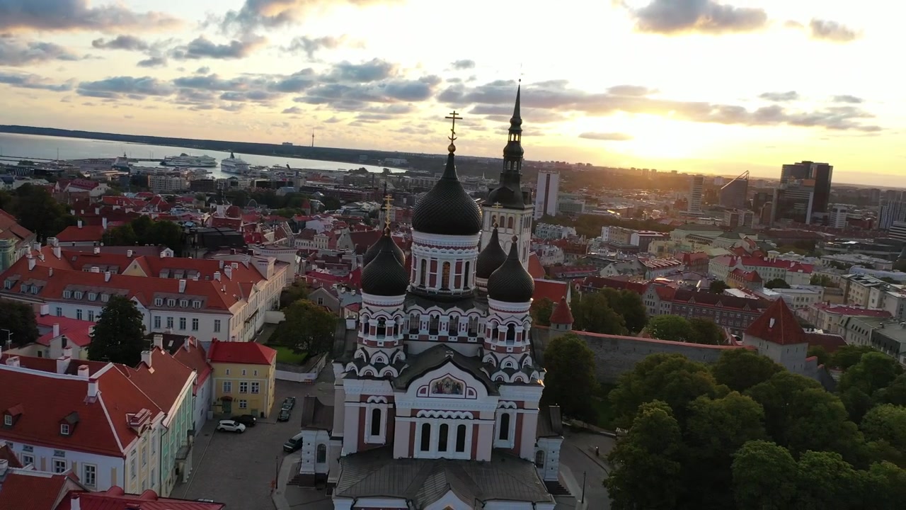 Filmato mozzafiato con drone del Centro Storico medievale di Tallinn al tramonto. L'inquadratura mostra la Collina di Toompea, la Cattedrale di Santa Maria e gli edifici dai tetti rossi sotto un cielo drammatico di nuvole rosa e arancioni.