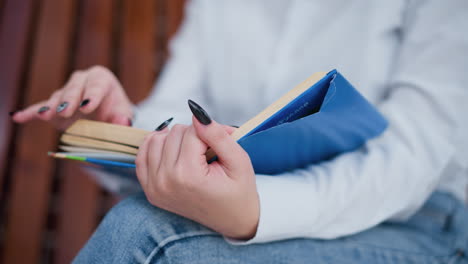 close-up of hand holding book with black polished nails, fingers gently flipping pages, person slightly blurred in background, creating a thoughtful reading moment with soft lighting