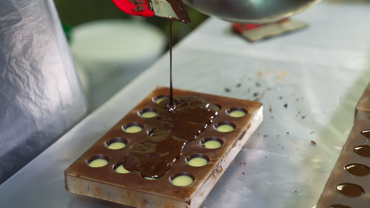 Chef pours the final layer of chocolate onto the mold. Melted chocolate is spread to make the bottoms of candies. Close up.