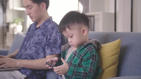 asian boy using smartphone while father working on laptop