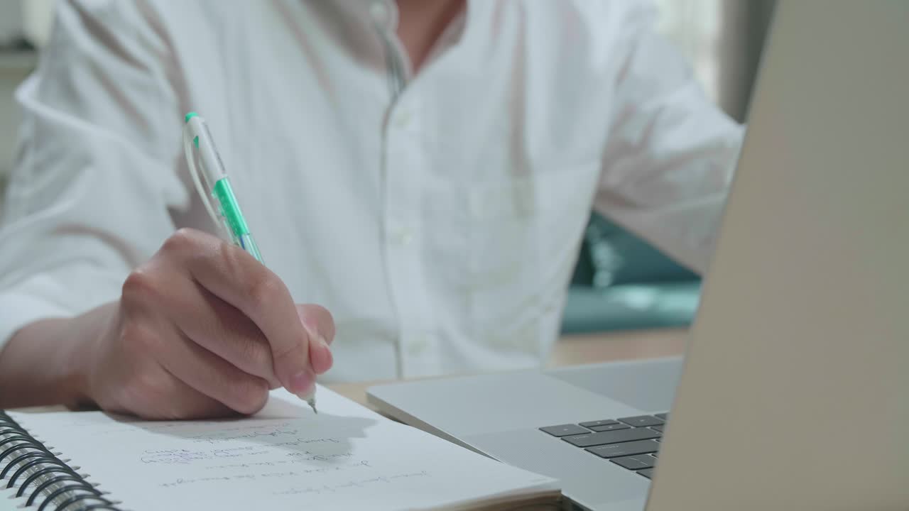 de cerca del hombre estudiante de la mano con la computadora escribiendo en el cuaderno mientras estudia en línea en casa