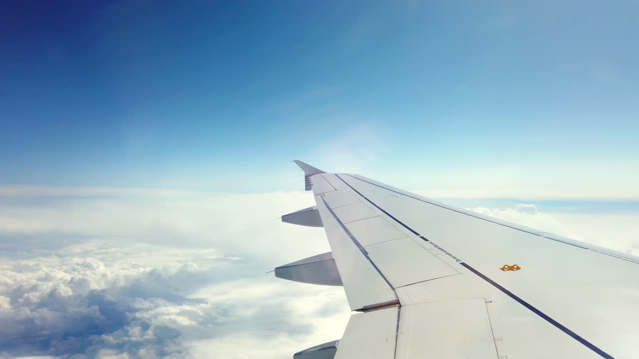 Soaring high above the clouds, the airplane wing cuts through the bright blue sky, showcasing a serene view of the sky and distant clouds on a clear day