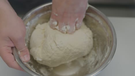 close-up of a baker's hands skillfully kneading dough in a large metal bowl.
