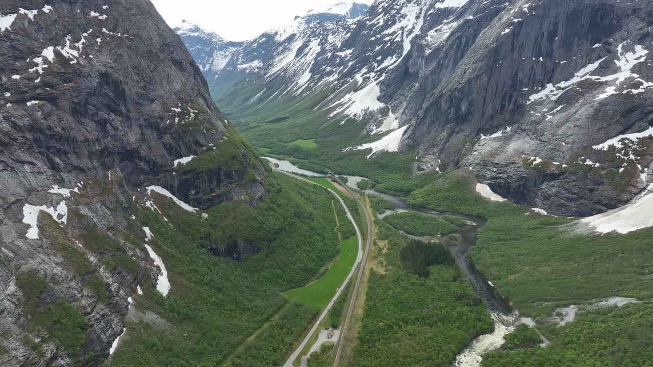 impresionante valle de romsdalen cerca de la pared montañosa de trollveggen en noruega - alta altitud aérea sobre el verde valle exuberante con carretera, ferrocarril y río - nieve en las montañas