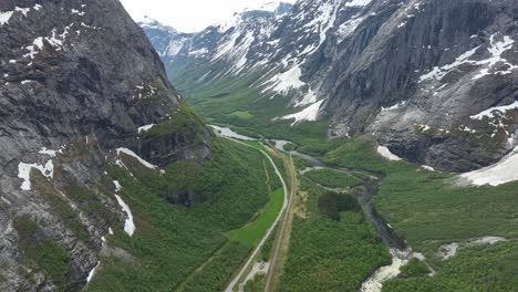 stunning romsdalen valley close to trollveggen mountain wall in norway - high altitude aerial above lush green valley with road, railway and river - snow in mountains