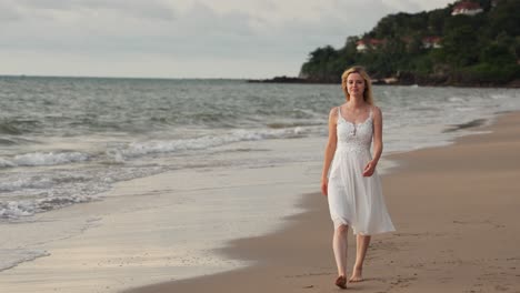 a slow motion shot of a girl wearing white dress walking at the tropical beach during sunset