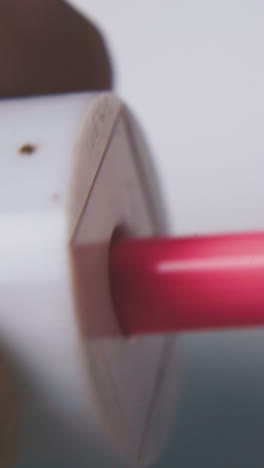 person sharpens bright pink pencil with white plastic sharpener on light background extreme close view