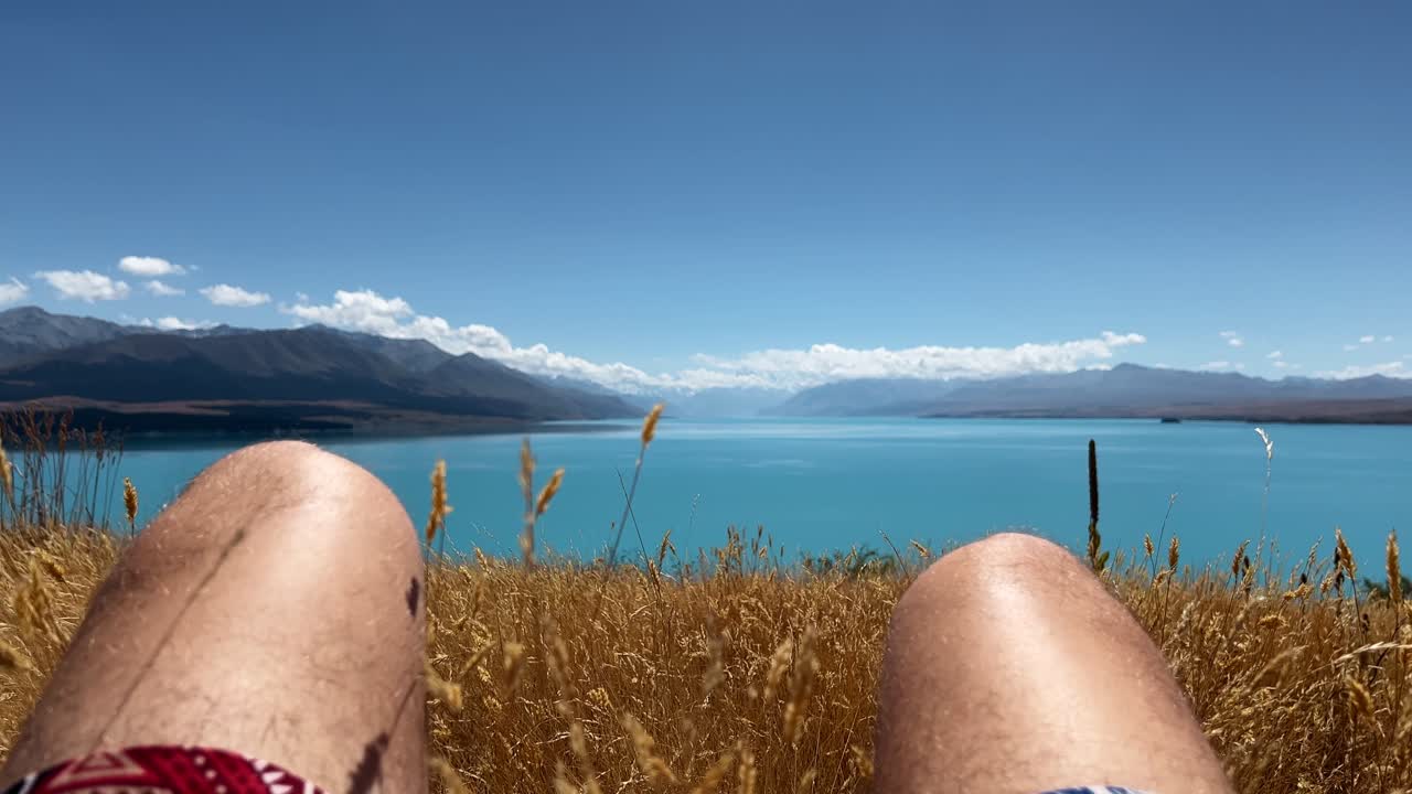 FPV footage of lying in dry grass above turquoise Lake Pukaki, New Zealand