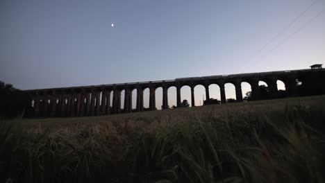 wide angle sliding shot of a train passing ouse viaduct at sunset with the moon