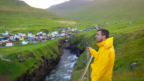 Male-tourist-in-yellow-jacket-at-viewpoint-over-Gjogv-village-and-canyon-in-a-windy-day