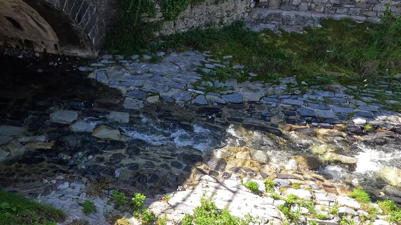Czysty strumień płynący pod kamiennym mostem.