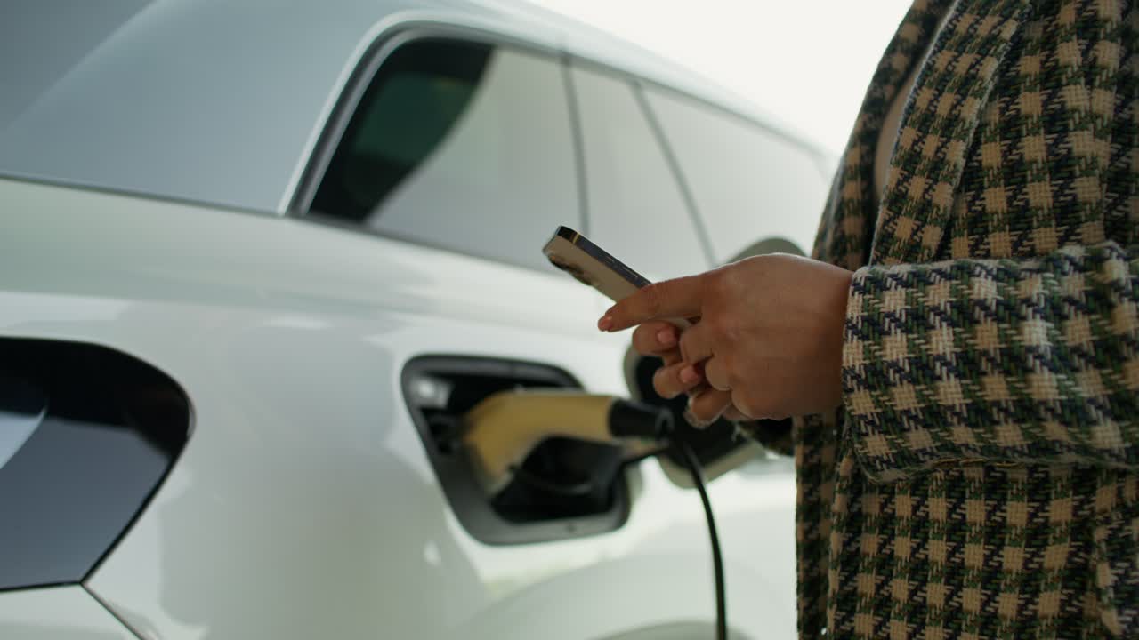 Elektrikli araç şarj istasyonunda akıllı telefon kullanan kadın