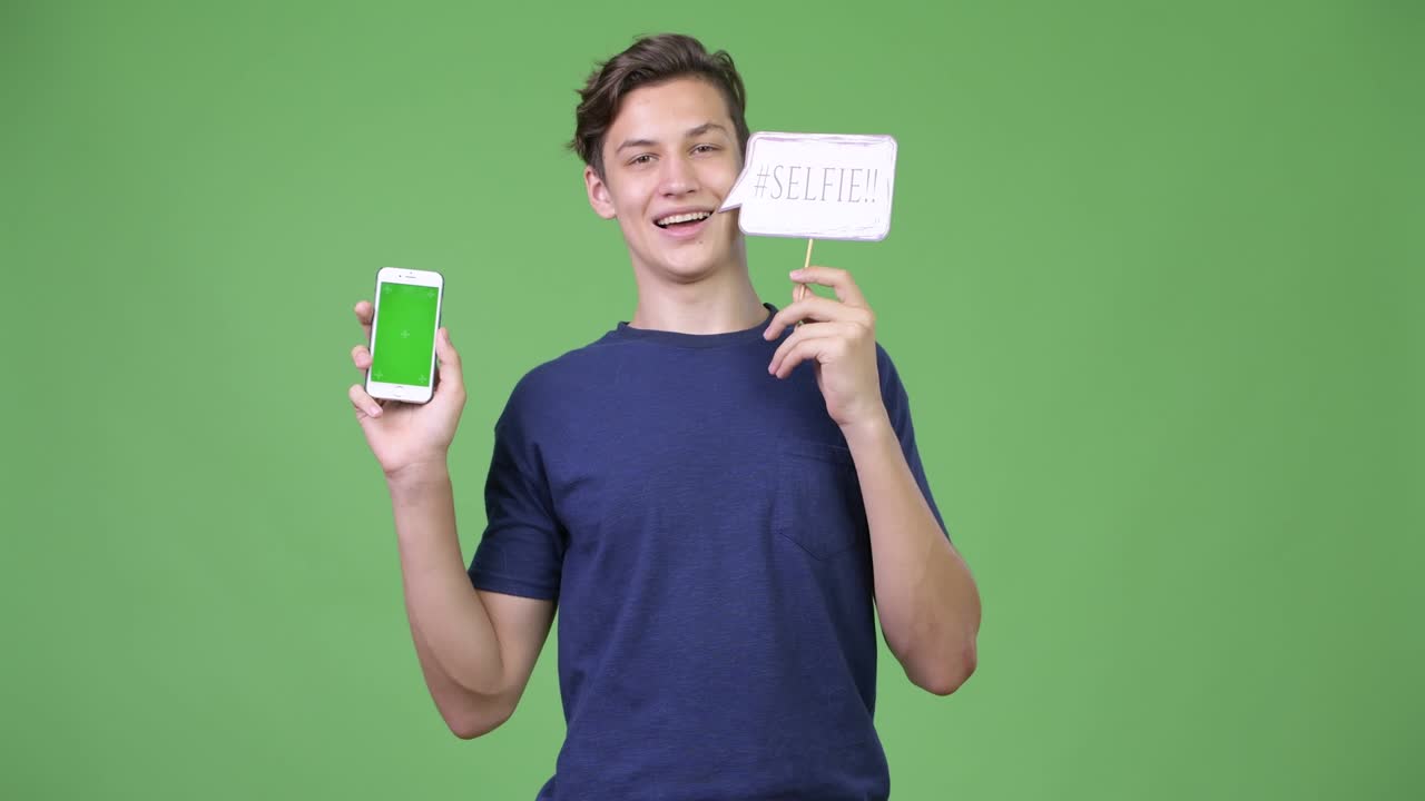 Giovane e bel ragazzo adolescente che mostra il telefono e un cartello "selfie"