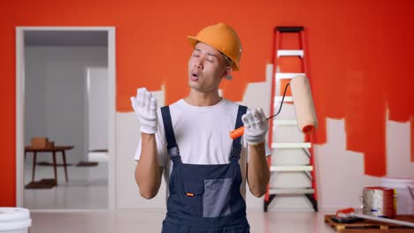 wondering asian man painter wearing safety helmet saying why and standing doubtfully with painting wall in room