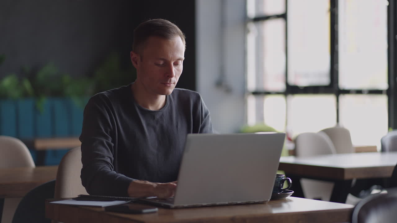 A serious man is a business student working studying sitting at a table and typing a message on a laptop. Typing text on the keyboard