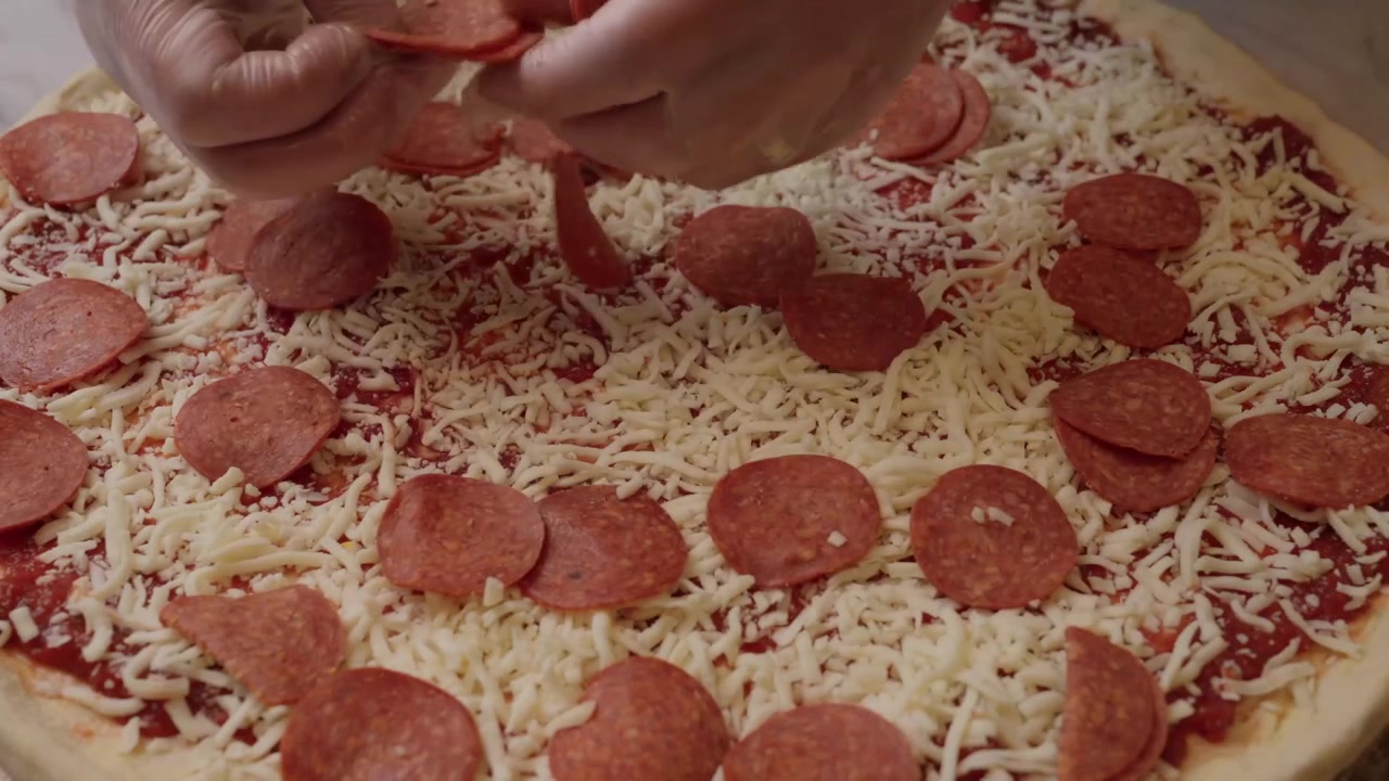 Primo piano di una pizza fatta in casa non cotta, condita con salsa di pomodoro rossa e abbondante mozzarella grattugiata su impasto crudo.
