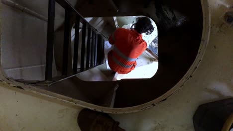 A-aerial-shot-of-low-angle-view-of-an-engineer-climbing-a-tower-on-an-industrial-steel-ladder-with-safety-cage