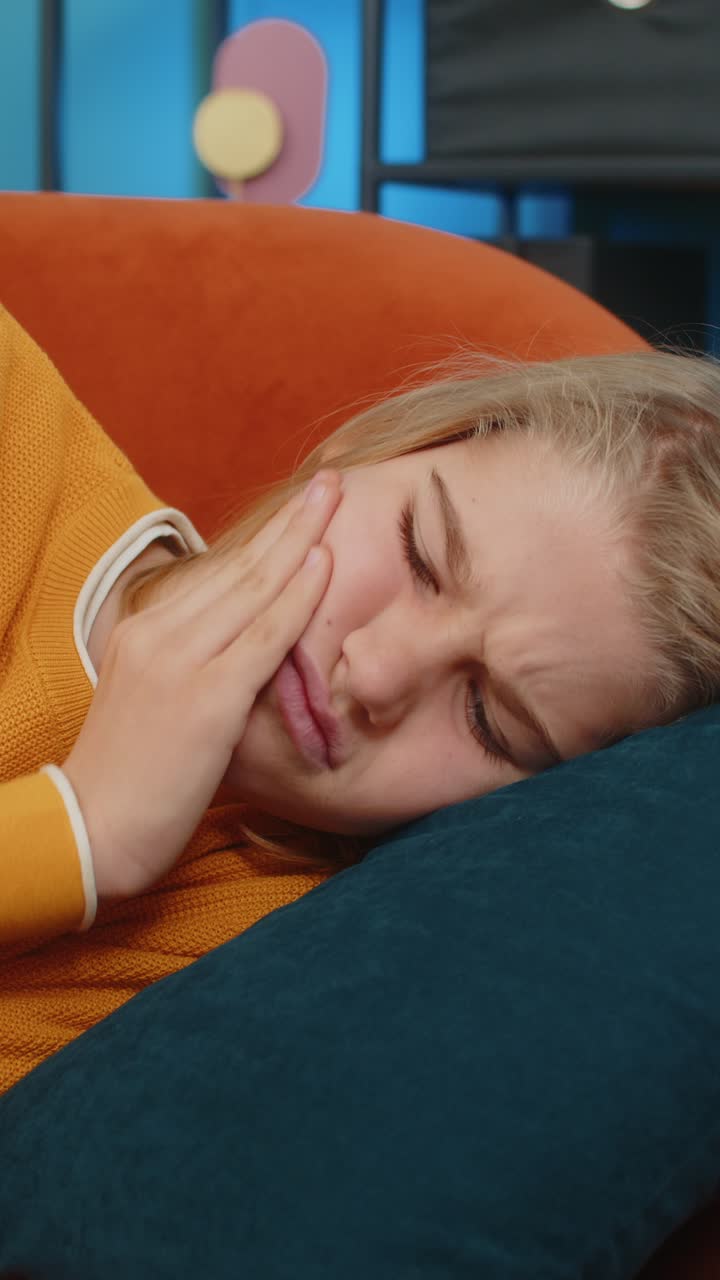 Teenager boy with toothache holding cheek suffering unbearable pain grimacing lying on sofa at home