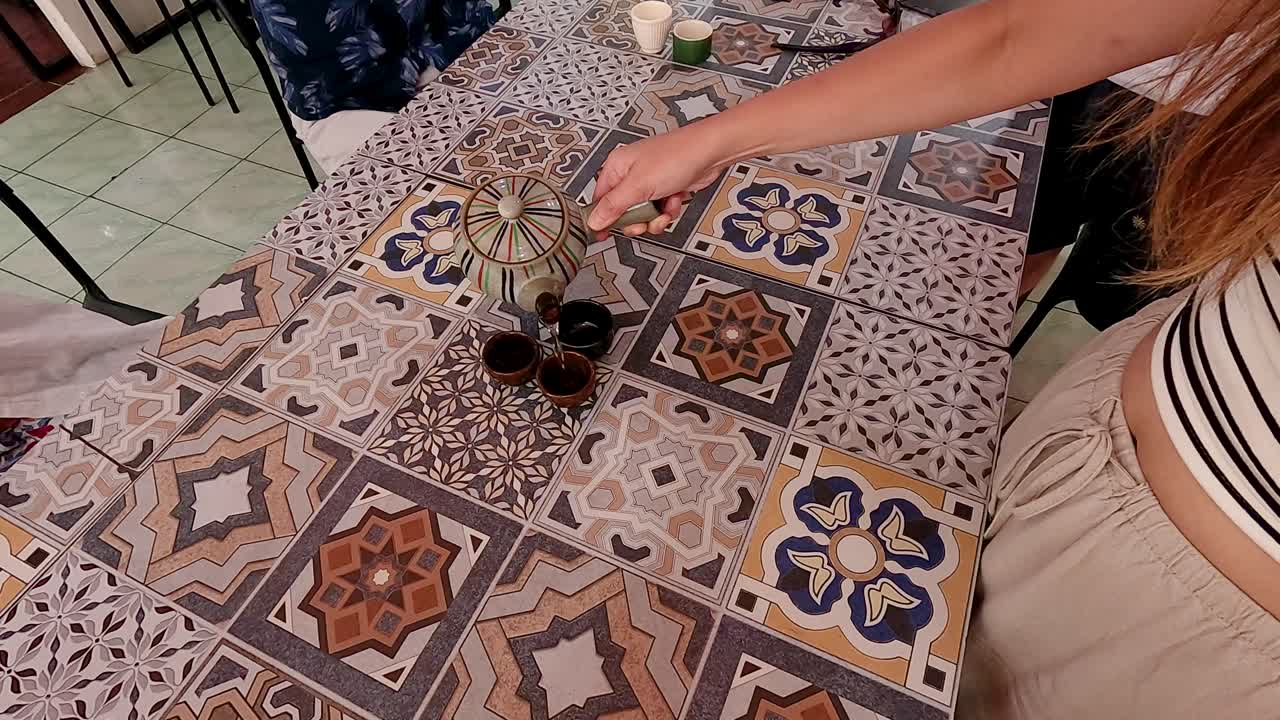 A person pours tea from a Chinese pot into cups on a patterned table in Phuket, Thailand