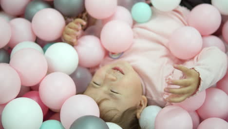 happy little girl dreamer lying in dry pool with colorful balls smiling