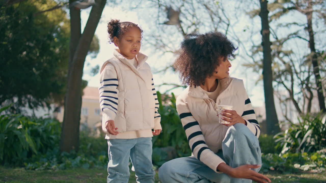 공원 주말에 비둘기에게 씨을 던지는 어린 소녀. 어머니와 함께 있는 아이