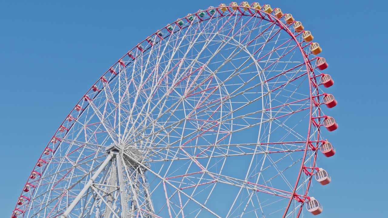 Close-up of the top half of a massive white and red Ferris wheel spinning slowly against a clear, bright blue sky