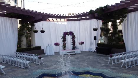 drone flying towards wedding stage, wedding ceremony under the open sky and a fountain at the center of the stage