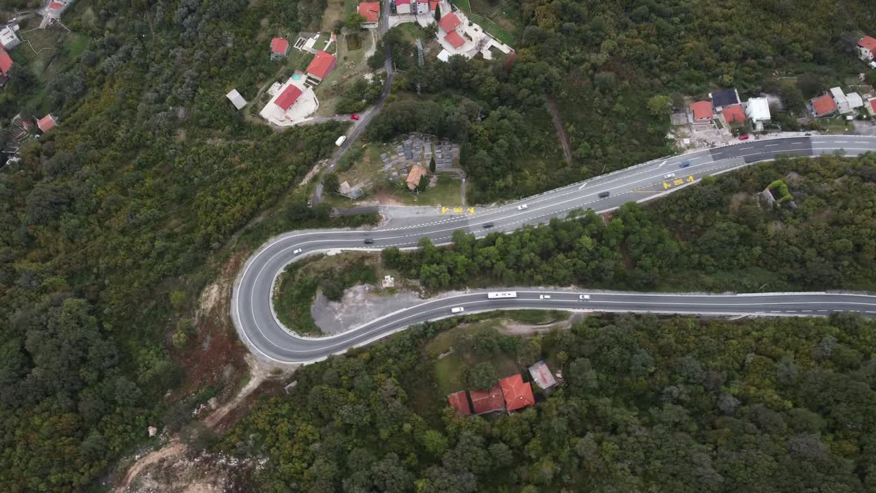 Drone footage of a winding road with a sharp hairpin turn cutting through forested hills in Minas Gerais, Brazil. Scattered homes and lush vegetation highlight rural life and terrain engineering