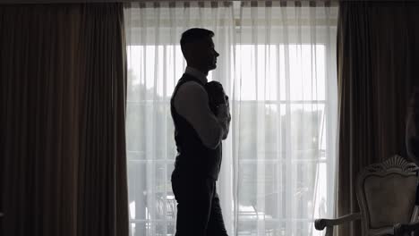 man in jacket fastens buttons, buttoning white shirt preparing to go out, walking near window