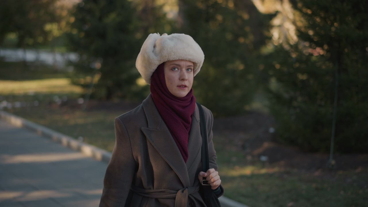 Giovane donna con cappotto invernale e cappello di pelliccia che cammina nel parco.