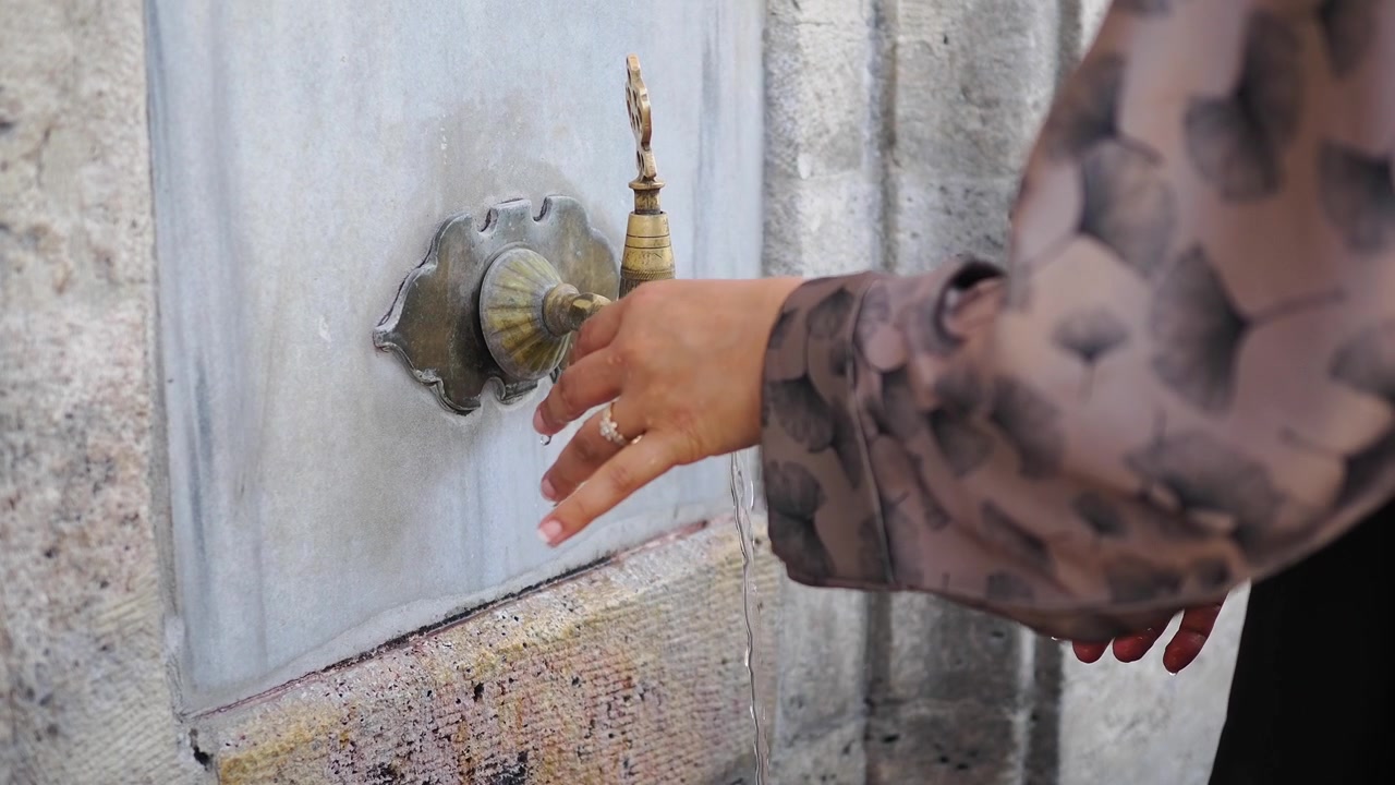 Person Washing Hands at Traditional Brass Fountain