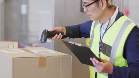 asian male worker wearing safety suit and scanning boxes in warehouse