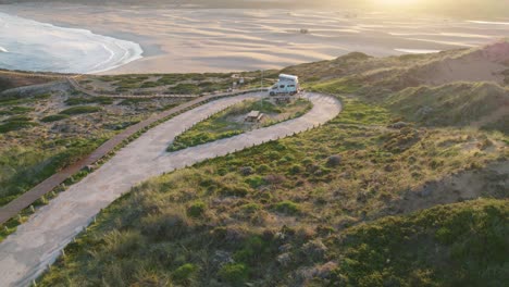 Aerial-view-towards-motorhome-parked-on-Bordeira-Portugal-hillside-coastline-overlooking-sunlit-seascape