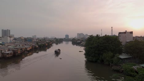 vietnamese river boat on canal with urban shacks in poor neighborhood of ho chi minh city showing houses and skyline in beautiful golden evening light