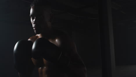 african american man wearing boxing gloves banging fists together in dark room