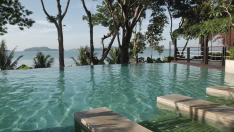 infinite swimming pool with background of natural sea and mountain view with some tree