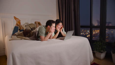 couple watching interesting movie on latop lying in bed at home