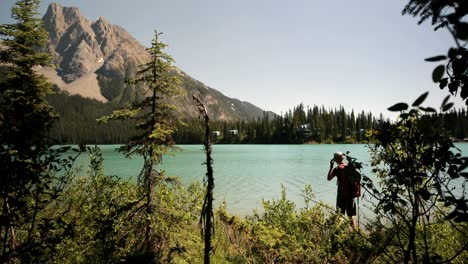 Rear-view-of-young-caucasian-male-hiker-with-backpack-standing-near-riverside-in-the-forest-4k