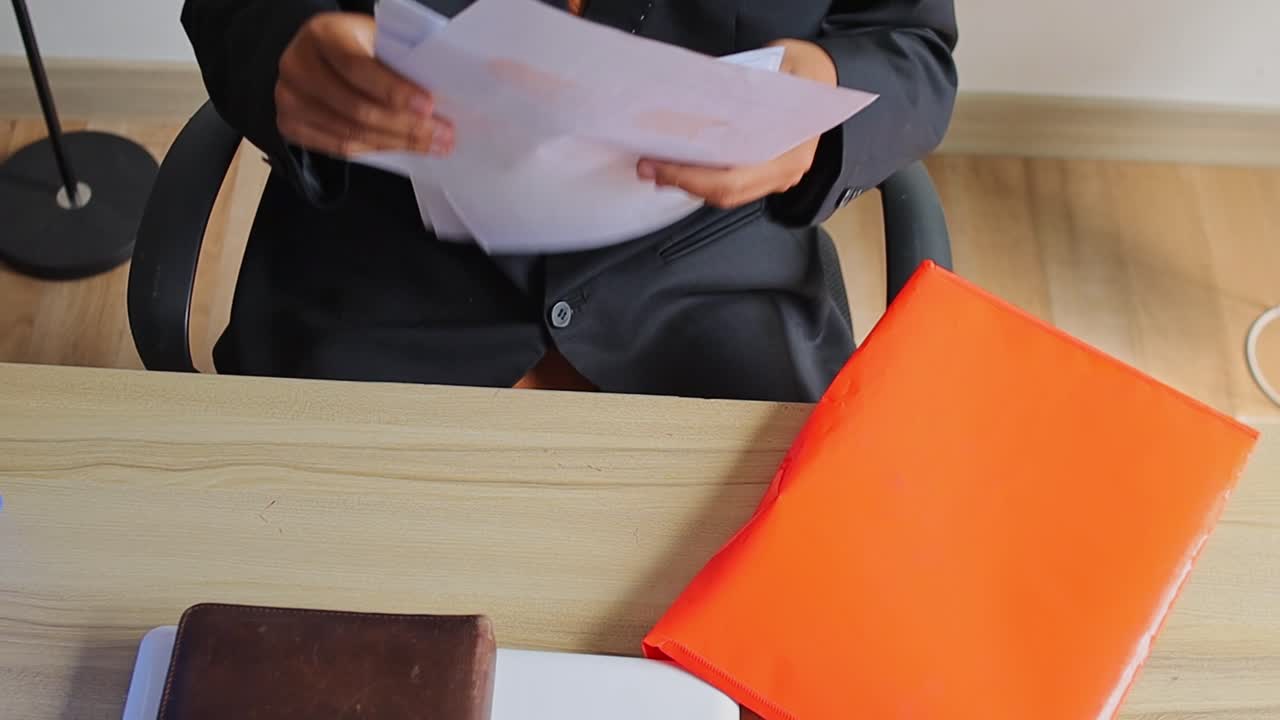 Businessman in suit reviewing documents out of orange folder at wooden desk