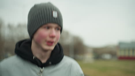 close-up of a young boy jogging on a track in a stadium, appearing focused from, the background is blurred, showing a football field