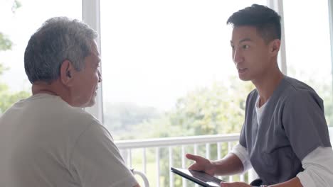 diverse male doctor with tablet discussing with senior male patient at home, slow motion