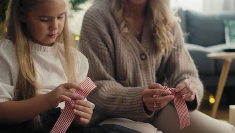 caucasian girl and mother wrapping christmas gifts with ribbon on the floor.